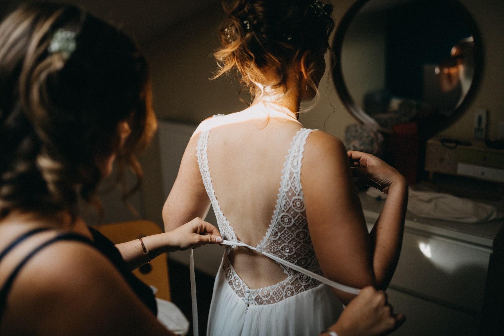 mariée qui se fait lacer la robe de mariée par sa témoin de mariage